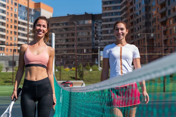 Due donne caucasiche sorridenti su un campo da tennis in una giornata estiva soleggiata. — Foto Stock