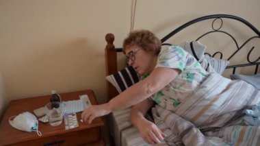 Hasta, yaşlı bir kadın yatağa uzanıp ilaç alıyor..