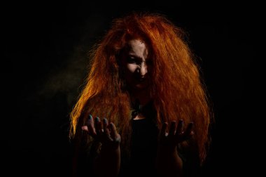 Portrait of an evil red-haired witch conjures in the dark. clipart