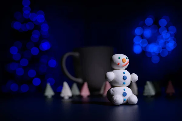 Милый снеговик и рождественские елки из зефира на фоне рождественских огней. Белая кружка горячего шоколада и сладостей. — стоковое фото