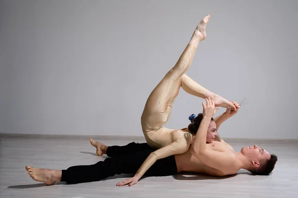 Акробатическая пара выполняет номер на белом фоне. Дуэт гимнасток репетирует спектакль при поддержке. Мужчина и очень гибкая женщина танцуют. — стоковое фото
