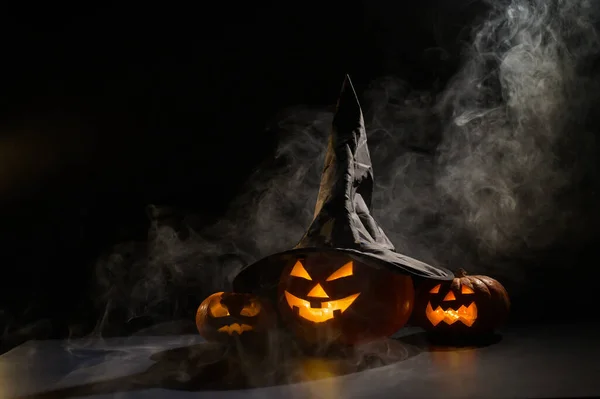 Trzy latarnie świecą w ciemności pośród mgły. Halloween dynia w kapeluszu czarownicy. — Zdjęcie stockowe