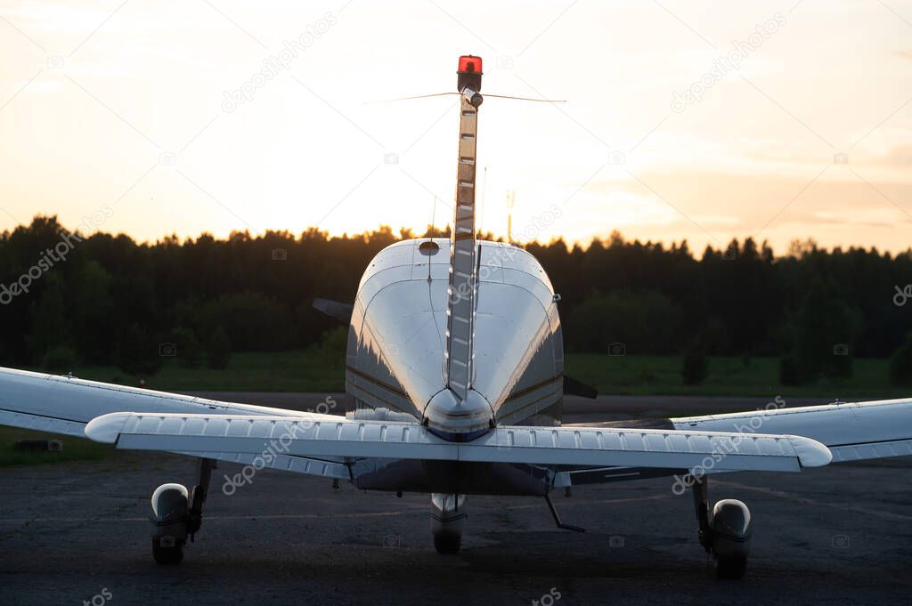 Quadruple aircraft parked at a private airfield. Rear view of a plane with a propeller on a sunset background.