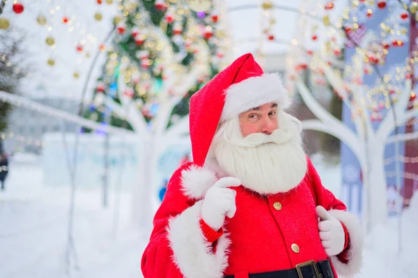 Retrato de un anciano vestido de santa claus sobre el fondo de un árbol de Navidad al aire libre. — Foto de Stock