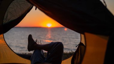Gün batımında sahilde bir turist çadırında kadın bacakları. Kadın nehir kenarında yürüyüş yapıyor ve kamp yapıyor..