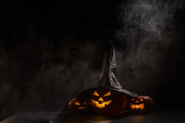 Tres faroles brillan en la oscuridad en medio de la niebla. Calabaza de Halloween en un sombrero de bruja. — Foto de Stock