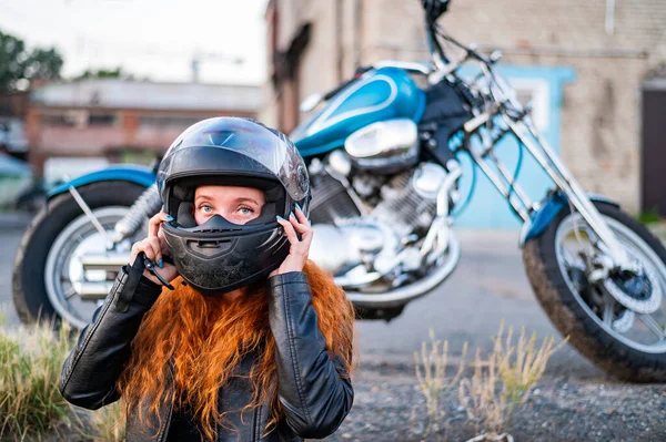 A red-haired woman puts on a helmet for safe motorcycle riding. — Stock Photo, Image