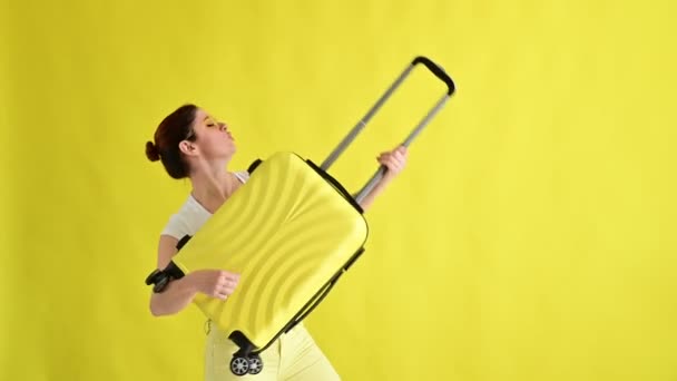 Beautiful caucasian woman fooling around with a suitcase on a yellow background. — Stock Video