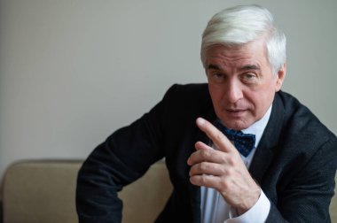Takım elbiseli yaşlı bir adam parmağını gösterir..