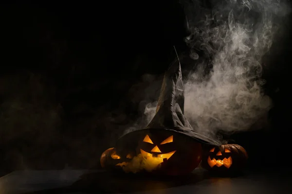Trzy latarnie świecą w ciemności pośród mgły. Halloween dynia w kapeluszu czarownicy. — Zdjęcie stockowe