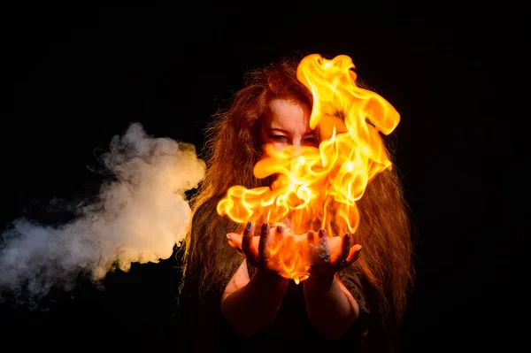 Uma bruxa ruiva malvada segura fogo em suas mãos. — Fotografia de Stock