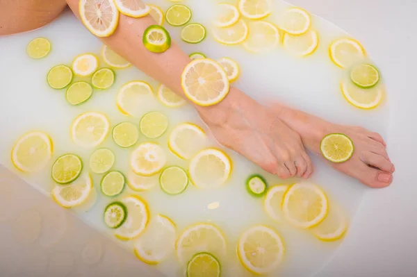 Femme méconnaissable prend un bain de lait avec des citrons et des citrons verts. Spa aux agrumes. Soins du corps. Blanchiment de la peau. jambes féminines vue du dessus. — Photo