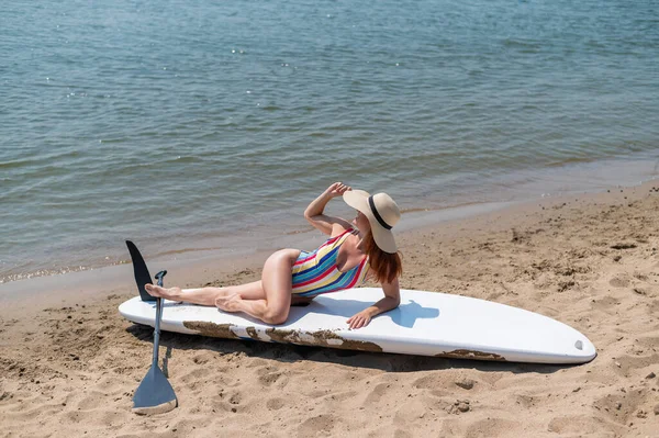 Žena v plavkách a klobouku pózuje na prkně na pláži.. — Stock fotografie