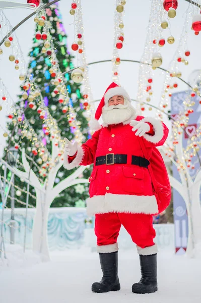 Retrato de un anciano vestido de santa claus sobre el fondo de un árbol de Navidad al aire libre. — Foto de Stock