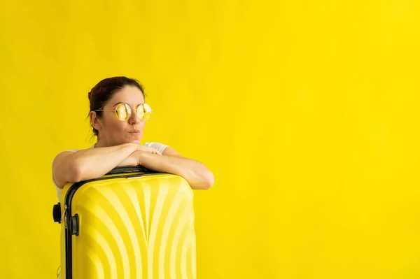 Eine Frau mit Sonnenbrille umarmt einen Koffer auf gelbem Hintergrund — Stockfoto