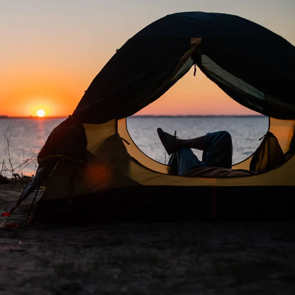 Une femme se trouve dans une tente touristique et profite du coucher de soleil sur la rivière. — Photo