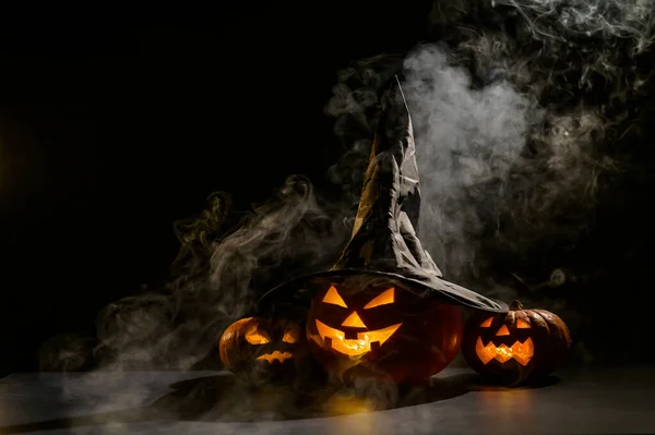 Tre jack o lyktor lyser i mörkret mitt i dimman. Halloween pumpa i en häxa hatt. — Stockfoto