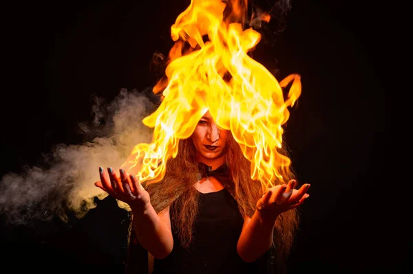 Een kwaadaardige roodharige heks houdt vuur in haar handen. — Stockfoto