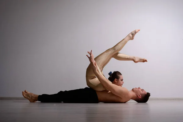 Un dúo de acróbatas mostrando un truco de pareja. Una mujer en un mono de gimnasia con un pie de mano sobre un hombre sin camisa se acuesta boca arriba. Artistas de circo muy flexibles. —  Fotos de Stock
