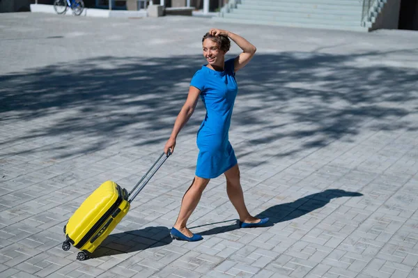 Gelukkige vrouw loopt door de straat met gele koffer met wielen — Stockfoto