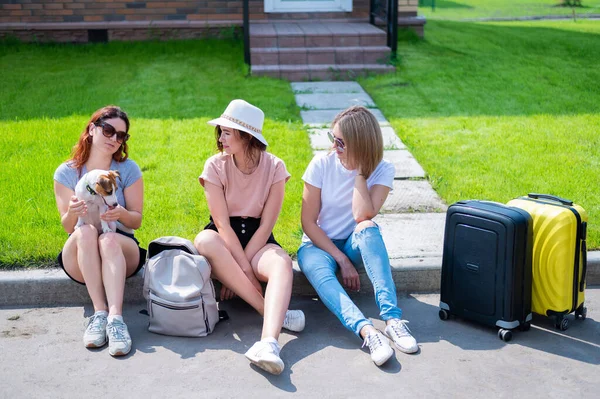 Drie blanke vrouwen en een hond gaan op reis. De meisjes laden hun koffers in de kofferbak van de auto. Zomervakantie concept samen met vriendinnen. — Stockfoto