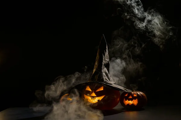 Sisin ortasında karanlıkta üç tane balkabağı feneri parlıyor. Cadılar Bayramı kabağı ve cadı şapkası.. — Stok fotoğraf