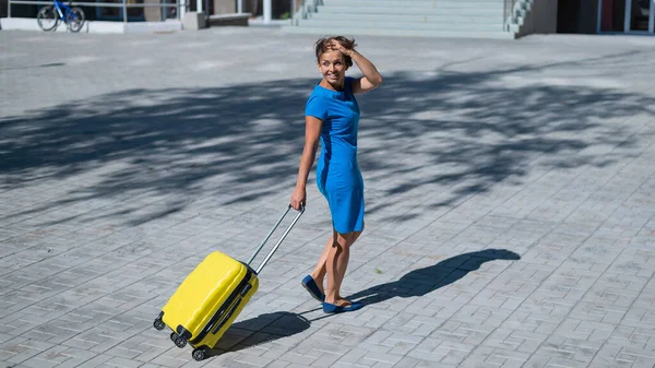 Glückliche Frau läuft mit gelbem Koffer mit Rädern die Straße entlang — Stockfoto