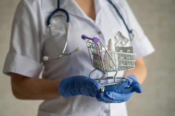 Um médico sem rosto coloca uma bolha de comprimidos em um carrinho de compras mini. — Fotografia de Stock