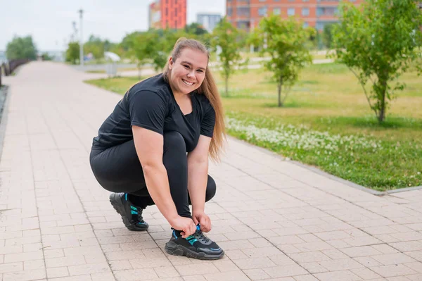 Eine dicke Frau im Trainingsanzug kauert und bindet ihre Schnürsenkel im Freien. — Stockfoto