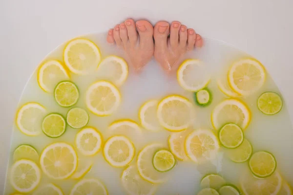 Fille prend un bain de lait avec des citrons et des citrons verts. Spa aux agrumes. Soins du corps. Blanchiment de la peau. Femmes pieds. — Photo