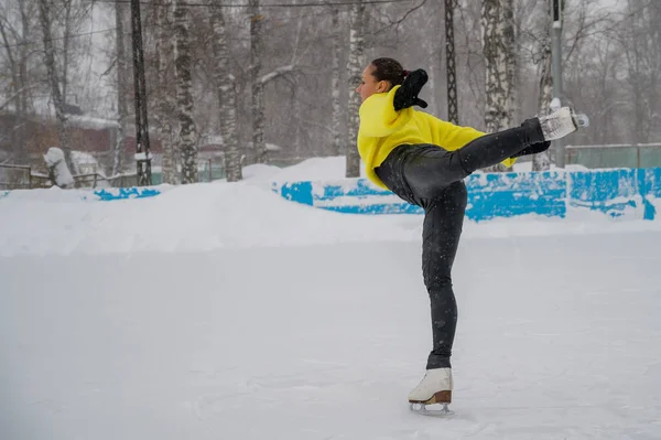 Un jeune patineur s'entraîne sur une patinoire extérieure en décembre. Une femme va faire des sports d'hiver. — Photo