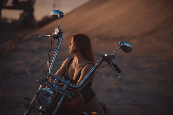 Vacker sexig kvinna i spets bodysuit och höga klackar sitter på en motorcykel på en industriell bakgrund — Stockfoto