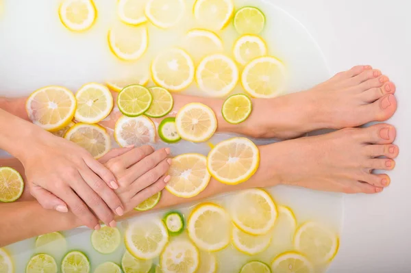 Belle jeune femme sans visage prend un bain avec des citrons au lait et de la chaux. Photo recadrée. Gros plan des mains et des pieds féminins dans un bain de blanchiment de la peau. — Photo