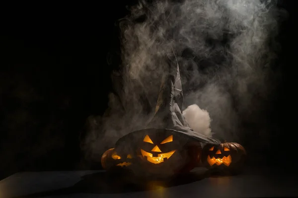 Three jack o lanterns glow in the dark amidst the fog. Halloween pumpkin in a witch hat. — Stock Photo, Image