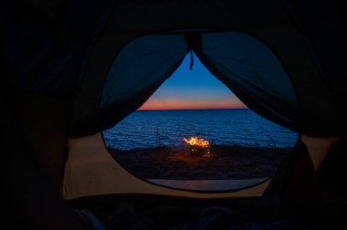 Gün batımında deniz kıyısında şenlik ateşinde bir turist çadırından manzara.