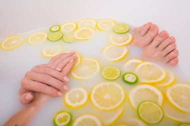 Meçhul, güzel bir kadın süt limonları ve limonla banyo yapıyor. Kesilmiş fotoğraf. Cilt beyazlatıcı banyoda kadın eli ve ayaklarının yakın çekimi.