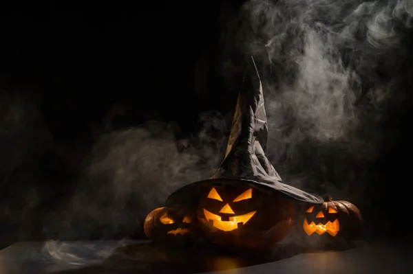 Τρία φανάρια λάμπουν στο σκοτάδι μέσα στην ομίχλη. Κολοκύθα Χάλογουιν σε μαγικό καπέλο. — Φωτογραφία Αρχείου