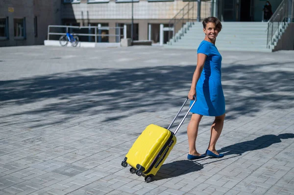 Gelukkige vrouw loopt door de straat met gele koffer met wielen — Stockfoto