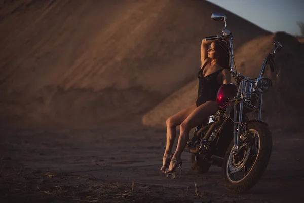 Mulher sexy bonita em terno de corpo de renda e saltos altos senta-se em uma motocicleta em um fundo industrial — Fotografia de Stock