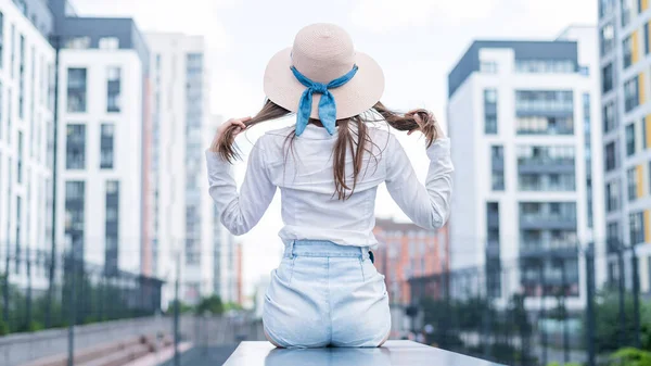 Vista posteriore di una donna con un cappello seduta sullo sfondo della città — Foto Stock