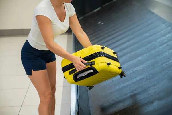 在机场候机楼，一个脸色苍白的女人从行李上卸下黄色的行李箱. — 图库照片