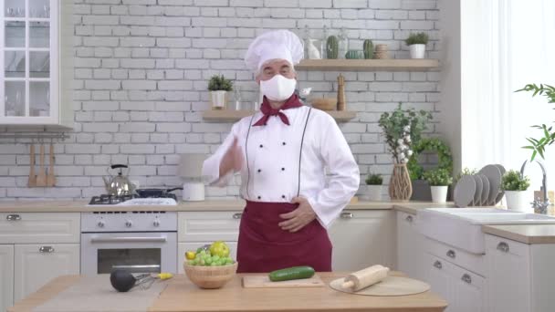 Mannelijke oudere chef-kok in een medisch masker in een keuken van het restaurant — Stockvideo