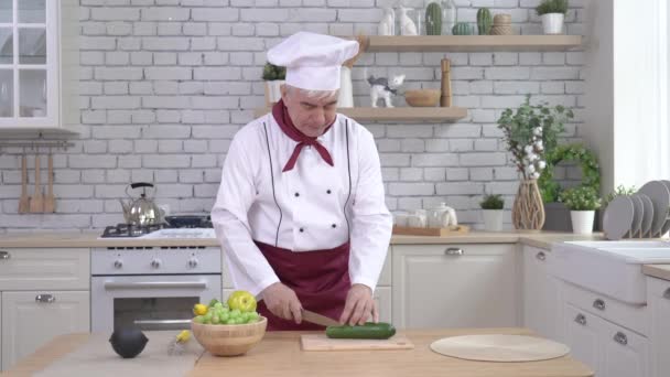Un bucătar în vârstă taie un castravete în bucătărie — Videoclip de stoc