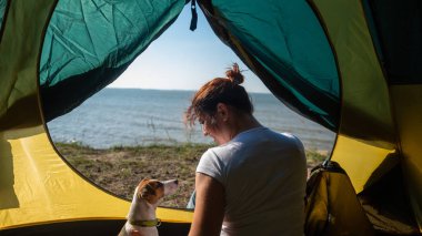 Bir kadın ve bir köpek deniz kenarındaki bir turist çadırında oturuyorlar. Doğada eğlence..