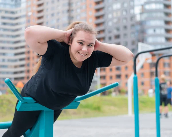 야외 경기장에서 운동 기구를 사용하여 허리 운동을 하는 뚱뚱 한 젊은 여자. — 스톡 사진