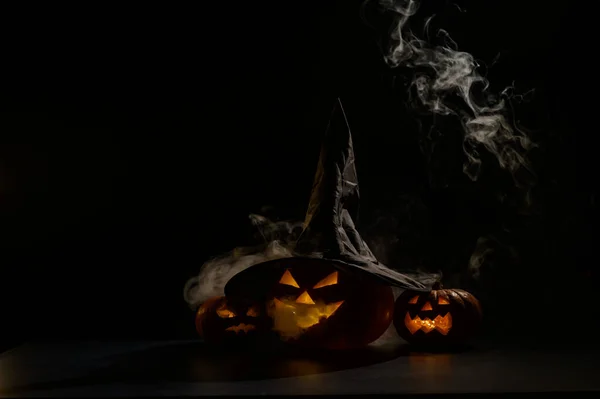 Three jack o lanterns glow in the dark amidst the fog. Halloween pumpkin in a witch hat. — Stock Photo, Image