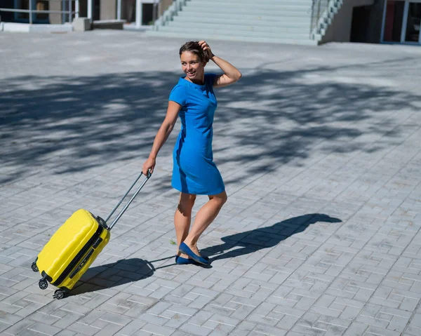 Gelukkige vrouw loopt door de straat met gele koffer met wielen — Stockfoto