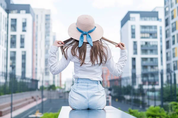Vista trasera de una mujer en un sombrero sentado en el fondo de la ciudad —  Fotos de Stock