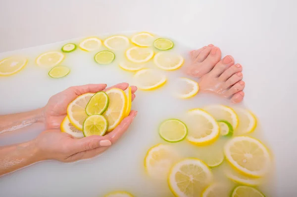 Krásná mladá žena bez tváře se koupe s mléčnými citróny a citrónem. Vystřižená fotka. Detailní záběr ženských rukou a nohou v bělící koupeli. — Stock fotografie