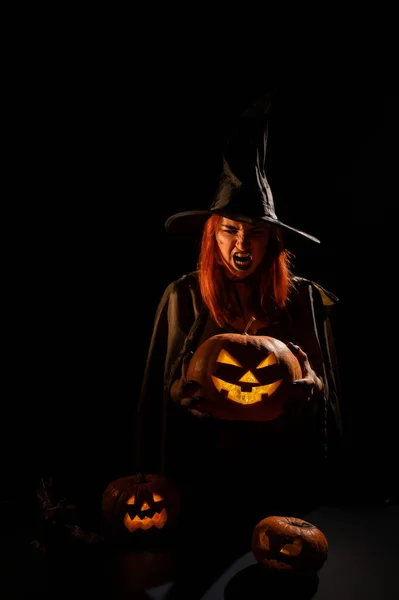 Zła wiedźma trzyma halloween jack-o-latarnię świecącą w ciemności — Zdjęcie stockowe